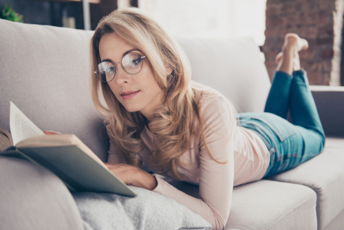 Young Woman with Glasses Laying on Couch and Reading