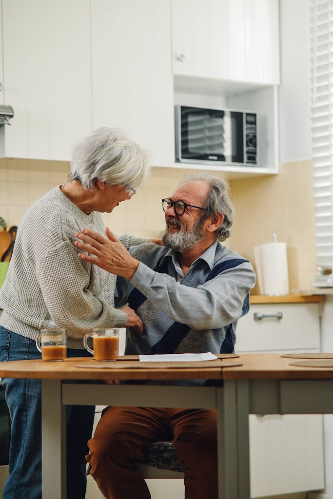 Senior couple smiling and embracing in a cozy kitchen setting.